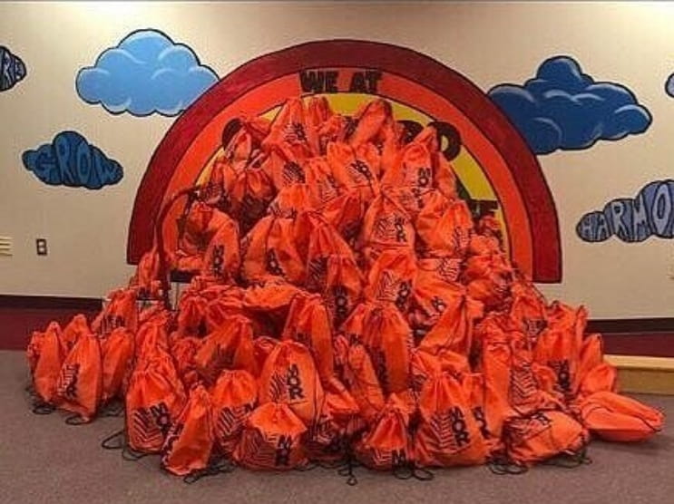 MOR Construction community outreach event with a large pile of branded orange giveaway bags for charity.